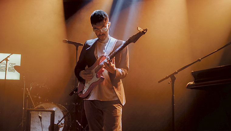 Claudio Suriano stående med guitat på orange baggrund