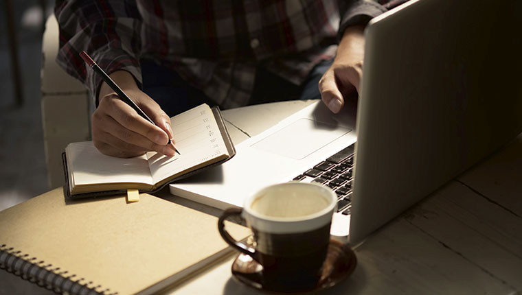 Hænder, kaffekop, PC og notesblok